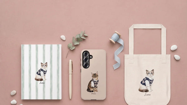 A dusty pink flat lay of a watercolor pet notebook, phone case and tote bag with a pen and eucalyptus
