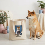 High School Photo Pet Tote Bag. A real red-and-cream Shiba Inu with pricked ears and a curled tail sitting on a pale wooden floor beside the natural canvas tote bag, which stands upright and open.
