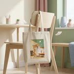 Homework Eaten Pet Tote Bag. The natural canvas tote bag slung over the back of a pale wooden chair in a bright minimal room.