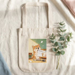 Homework Eaten Pet Tote Bag. Overhead flat lay of the natural canvas tote bag on cream linen with a sprig of eucalyptus beside it.