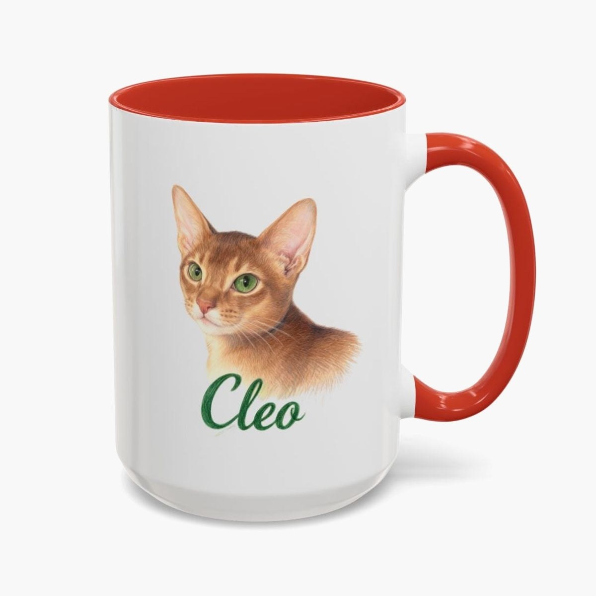 Colored pencil portrait of a ginger Abyssinian cat on a 15 oz mug with a red handle, with the name "Cleo" drawn below.