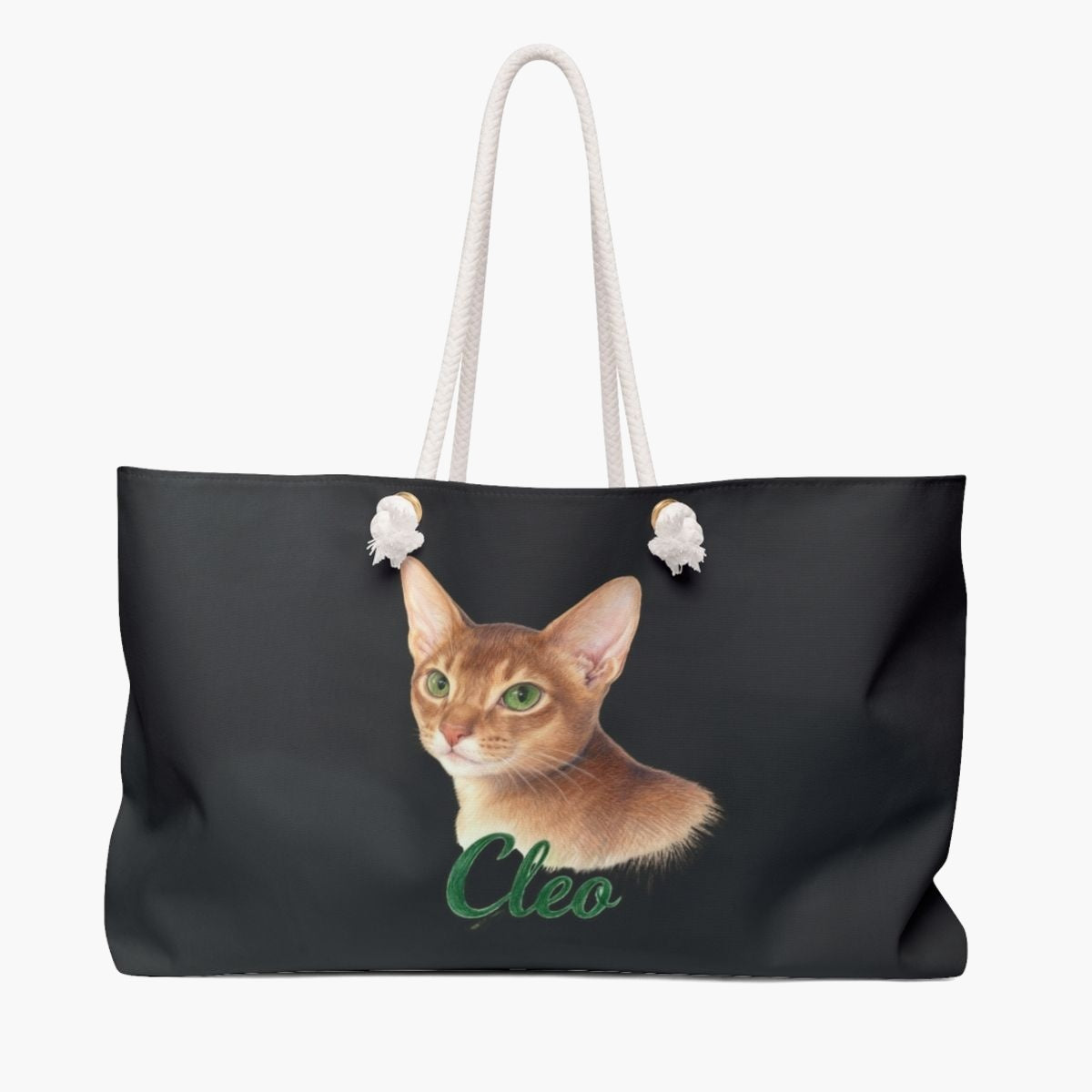 Colored pencil portrait of a ginger Abyssinian cat on a charcoal gray weekender bag with white rope handles, with the name "Cleo" drawn below.