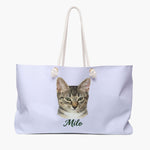 Colored pencil portrait of a tabby cat on a lavender weekender bag with white rope handles, with the name "Milo" drawn below.