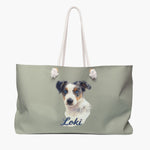 Colored pencil portrait of a blue merle Australian shepherd puppy on a sage weekender bag with white rope handles, with the name "Loki" drawn below.