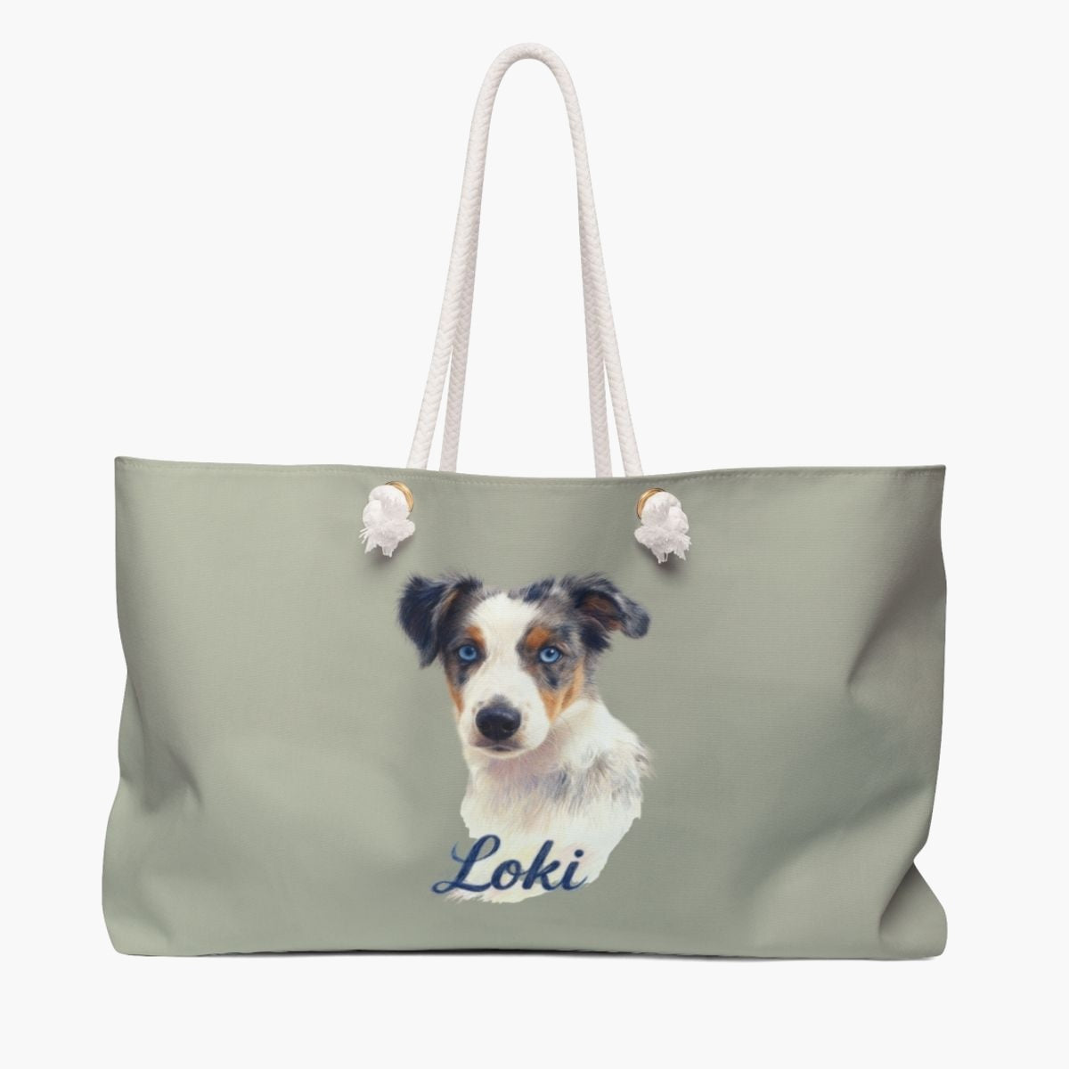 Colored pencil portrait of a blue merle Australian shepherd puppy on a sage weekender bag with white rope handles, with the name "Loki" drawn below.