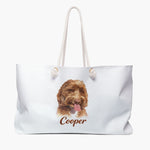 Colored pencil portrait of an apricot labradoodle on a soft white weekender bag with white rope handles, with the name "Cooper" drawn below.