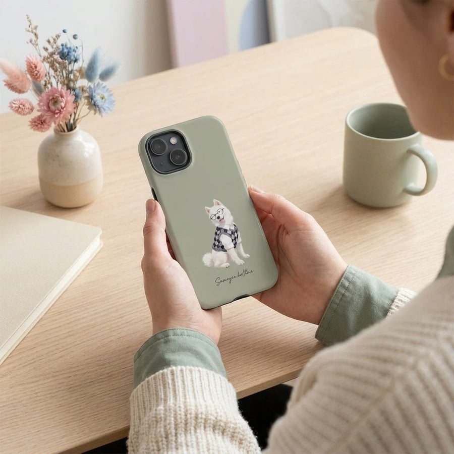 Student Watercolor Pet Phone Case. A person holding the phone case in both hands over a pale oak desk, cropped at the chin, looking down at it.
