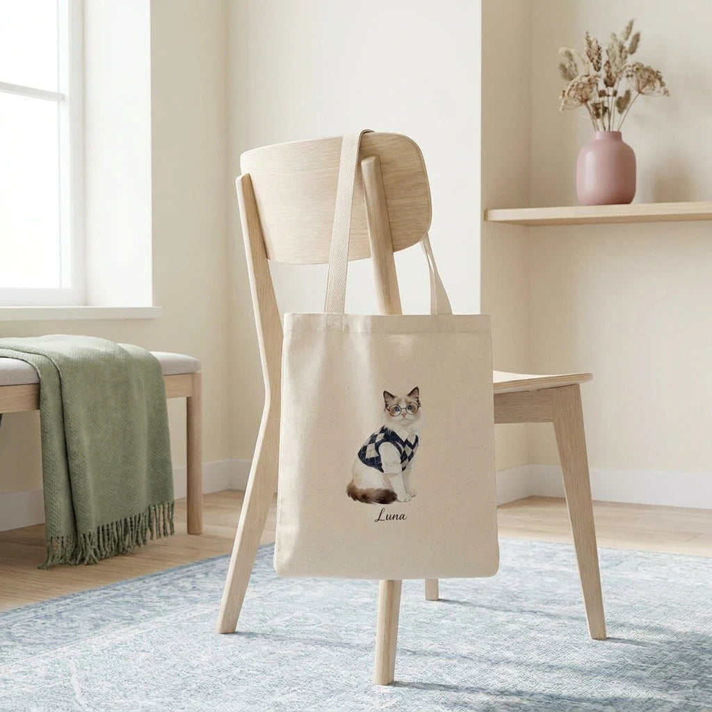 Student Watercolor Pet Tote Bag. The natural canvas tote bag slung over the back of a pale wooden chair in a bright minimal room.